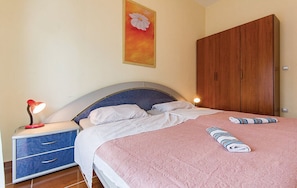 Un dormitorio con cama, mesita de noche con lámpara, armario de madera y un cuadro en la pared.