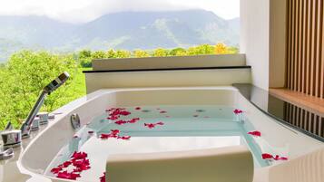 Una bañera con pétalos de rosa, una ventana con vistas a montañas y un panel de madera.