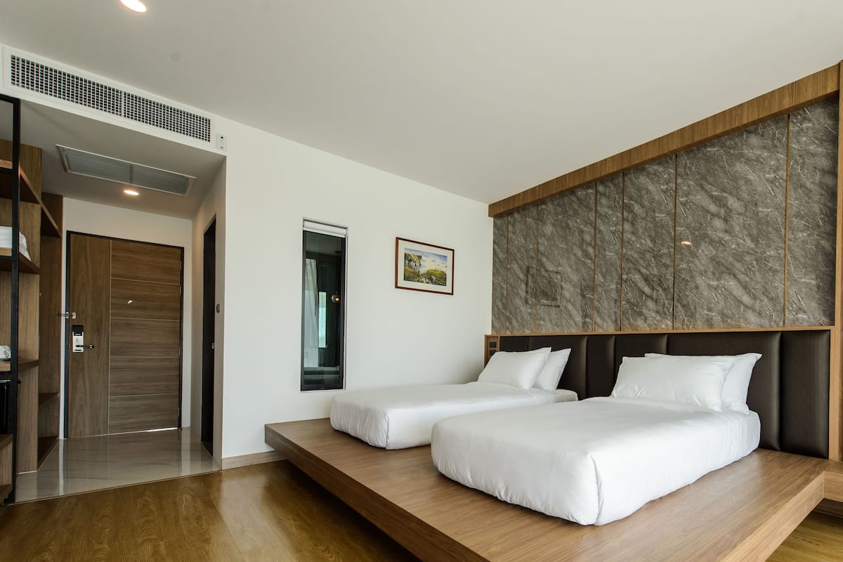 A modern hotel room with two beds, a marble accent wall, wooden paneling, and a built-in shelf.