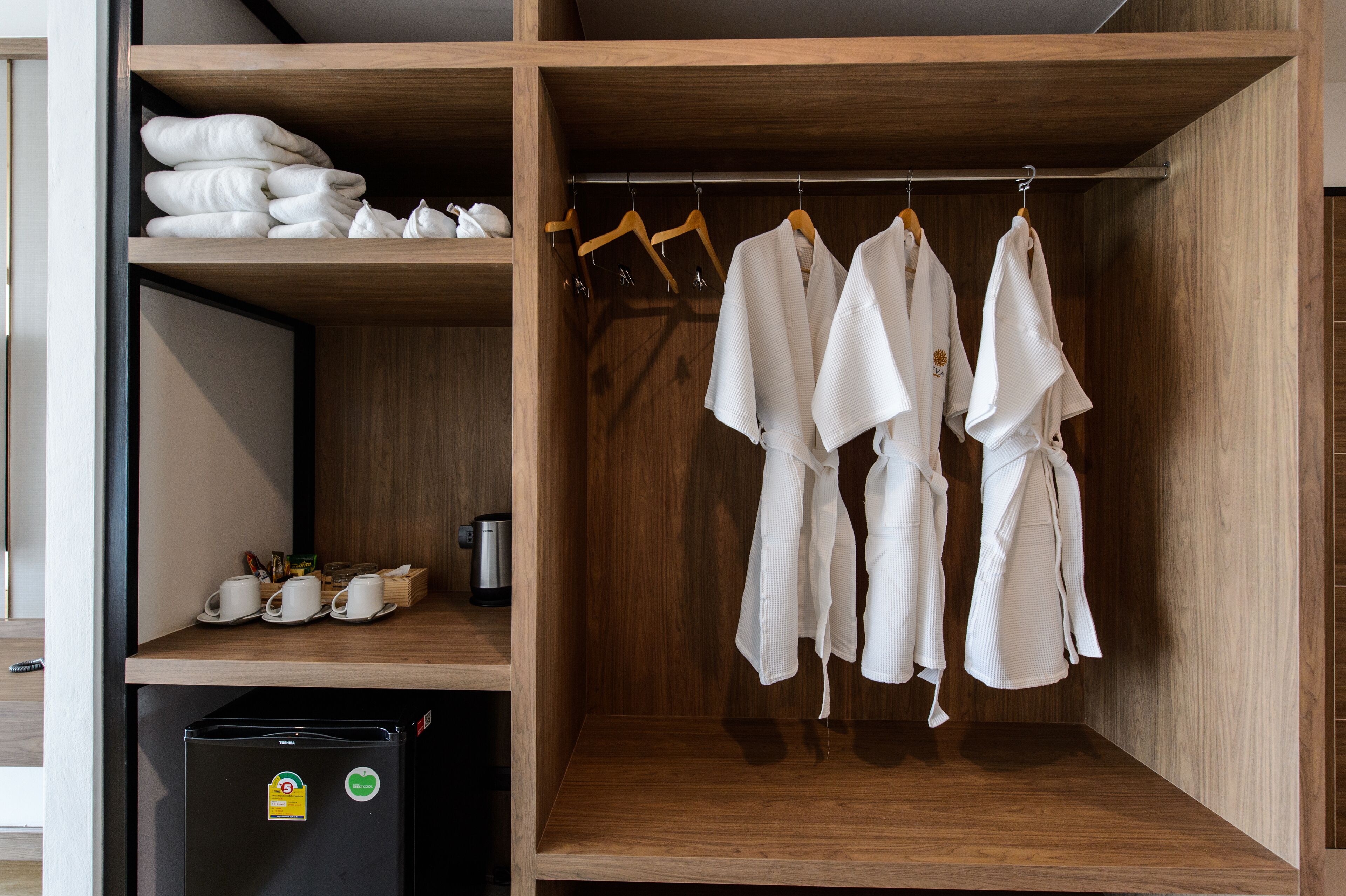 A wooden wardrobe with multiple shelves, a hanging rack, and a small refrigerator.