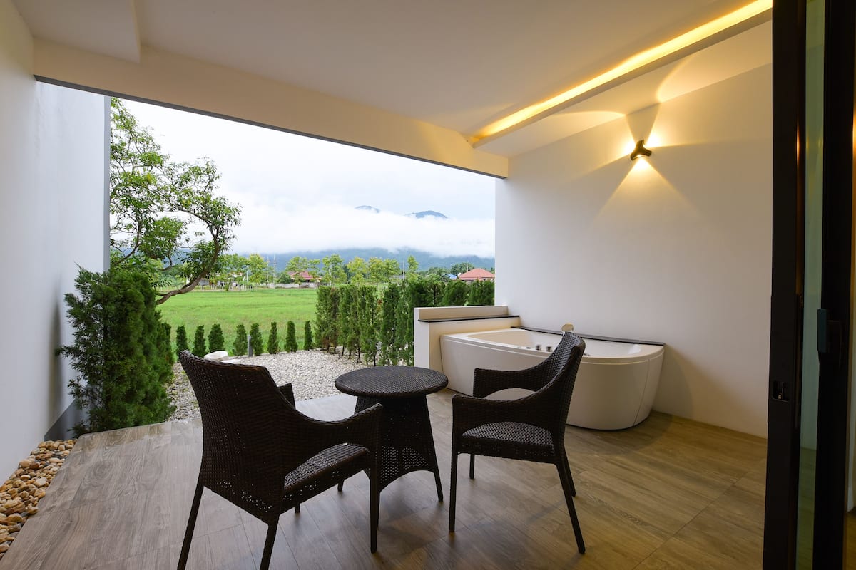 A modern balcony with wicker furniture, a built-in bathtub, and a view of a green landscape.