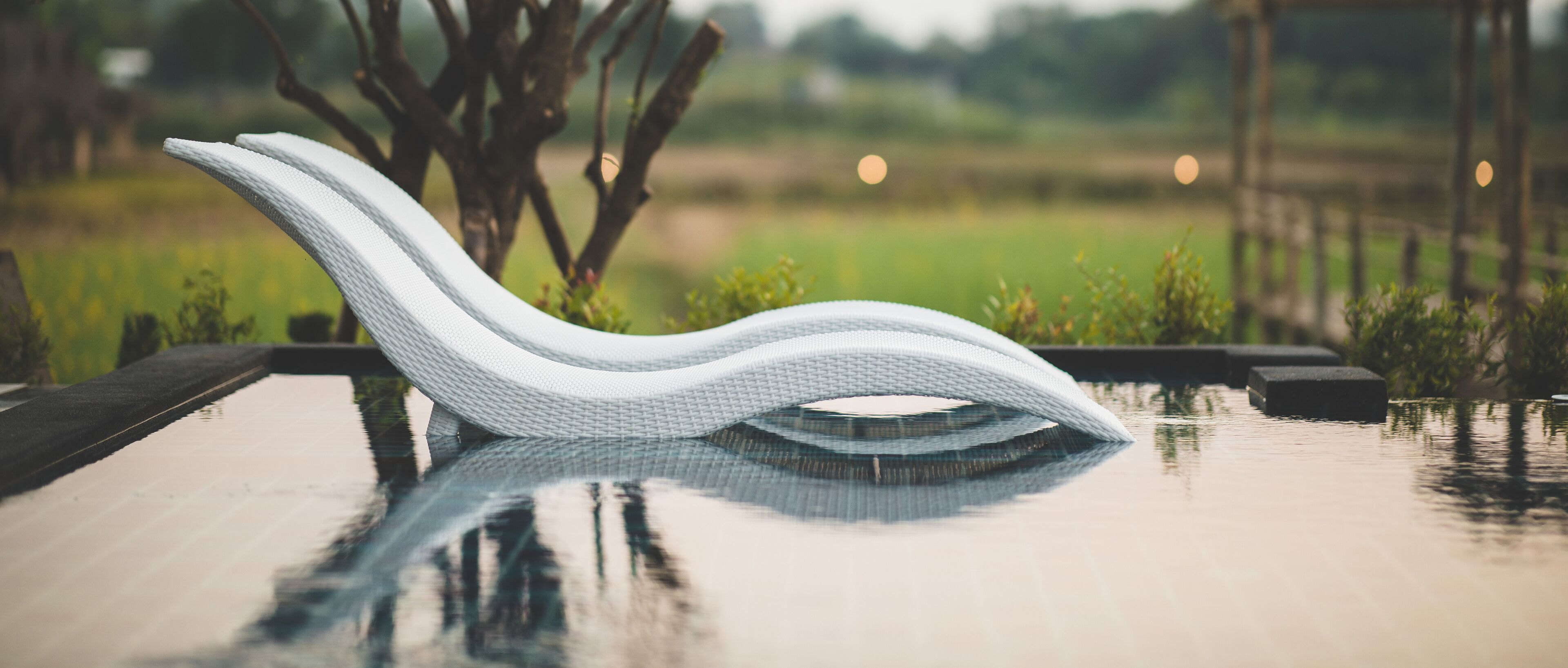 A modern, white, wavy-designed chair by a reflective pool with a blurred natural landscape in the background.