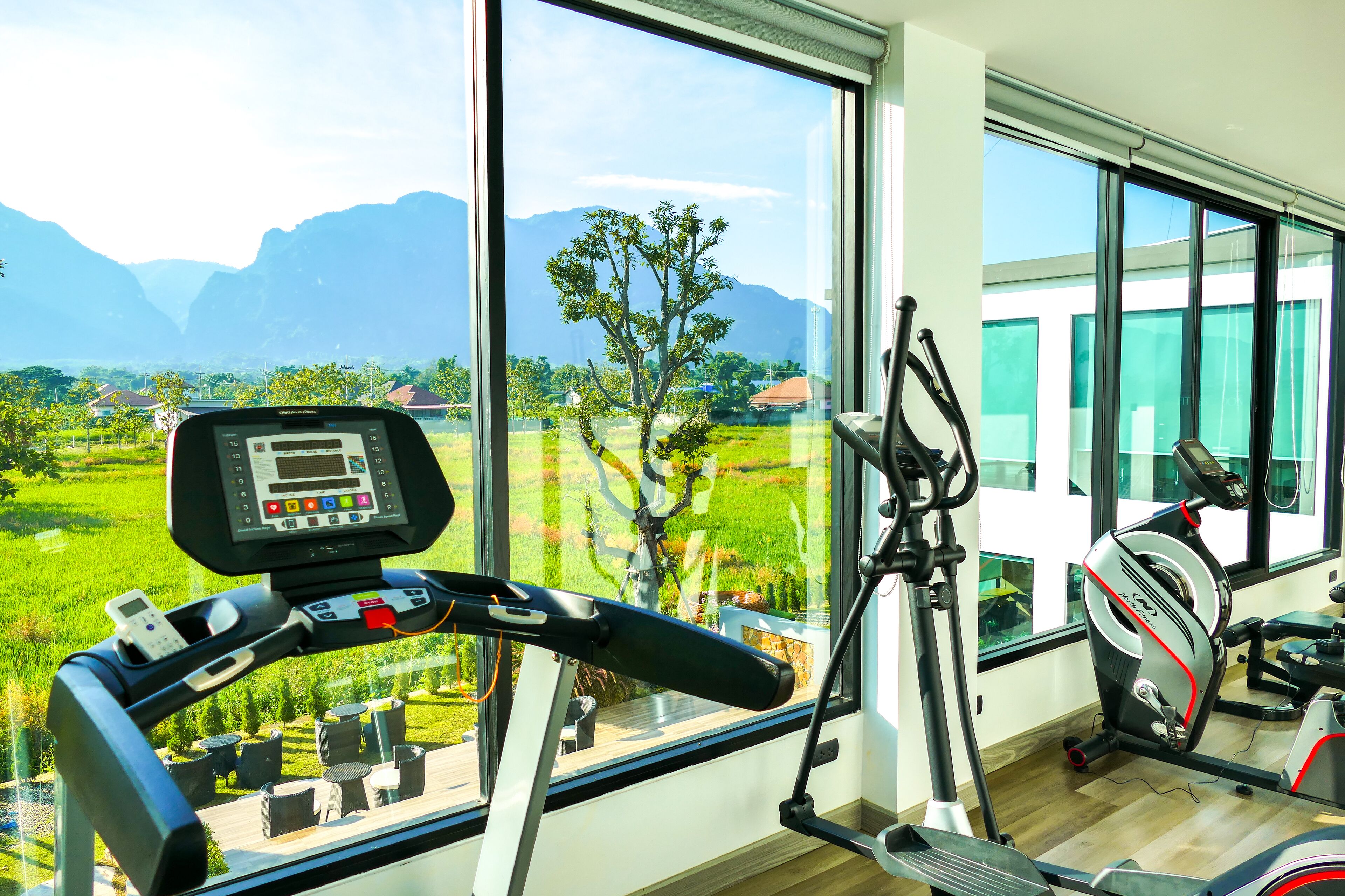 A home gym with a treadmill, stationary bike, and exercise equipment, overlooking a scenic view of mountains and greenery.