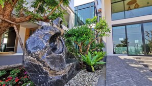 A modern building with large glass windows, a stone sculpture, and a variety of plants. - TEVA Valley Resort (Mae Sai)