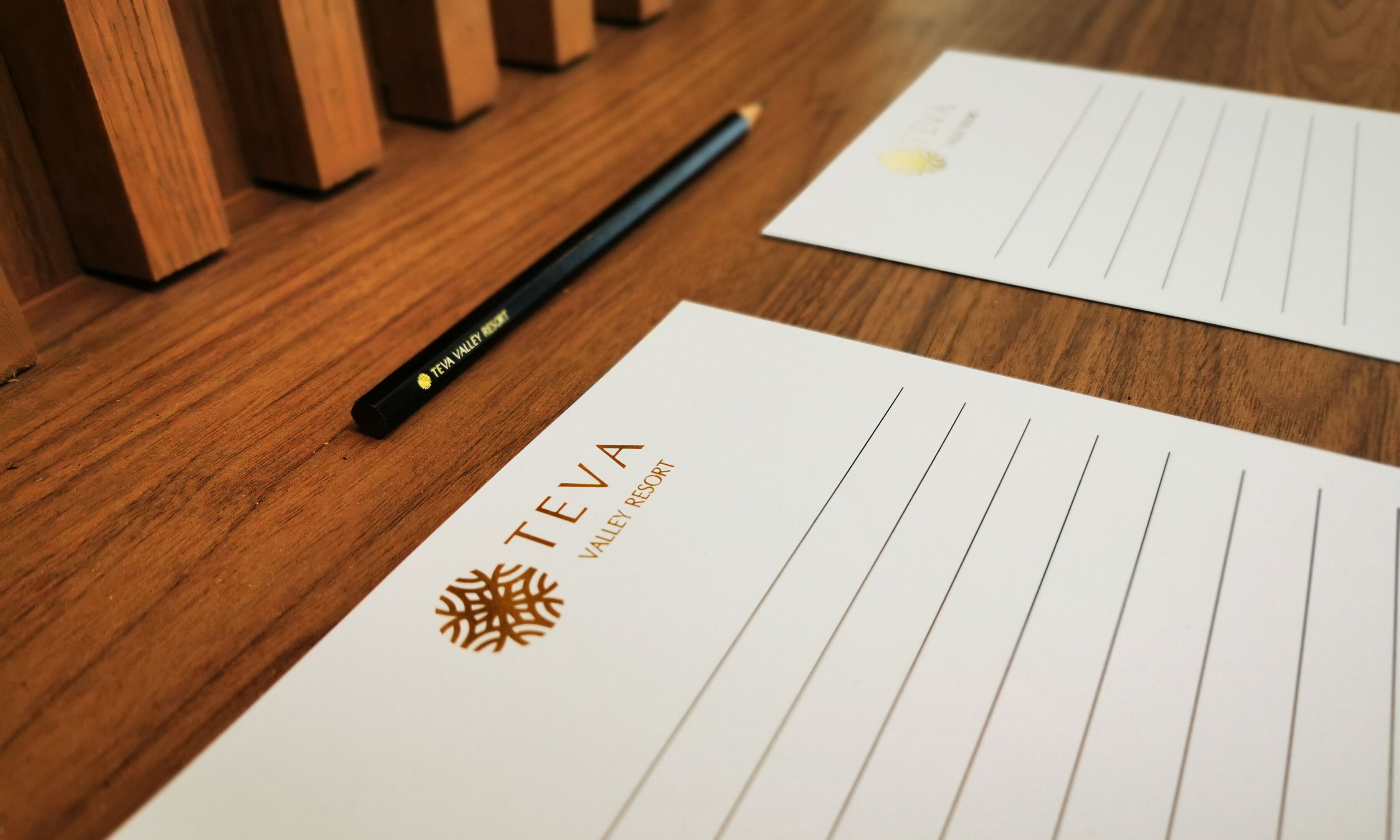 Ein Holztisch mit Schreibutensilien, darunter ein Stift und ein Notizblock mit dem Logo "TEVA VALLEY RESORT".