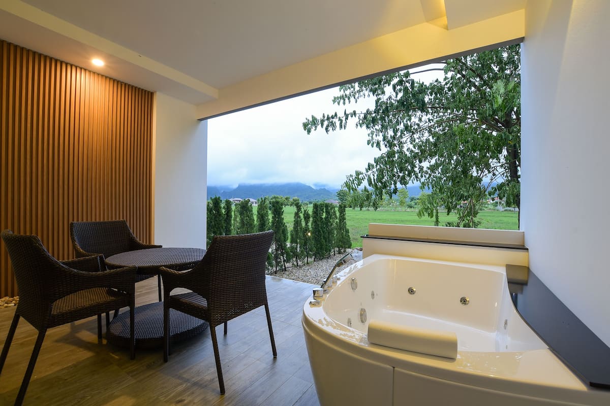 A modern bathroom with a bathtub, a window with a view of greenery and mountains, and wicker furniture.
