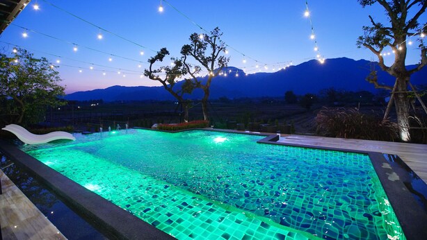 A swimming pool with string lights, surrounded by trees and a mountainous backdrop. - TEVA Valley Resort (Mae Sai)