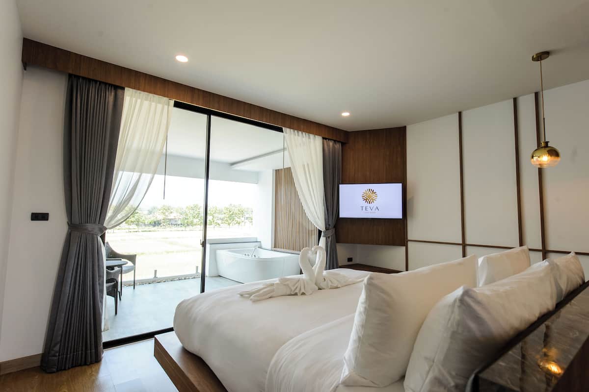 A modern hotel room with a large bed, a TV mounted on the wall, and a view of the outdoors through a sliding glass door.