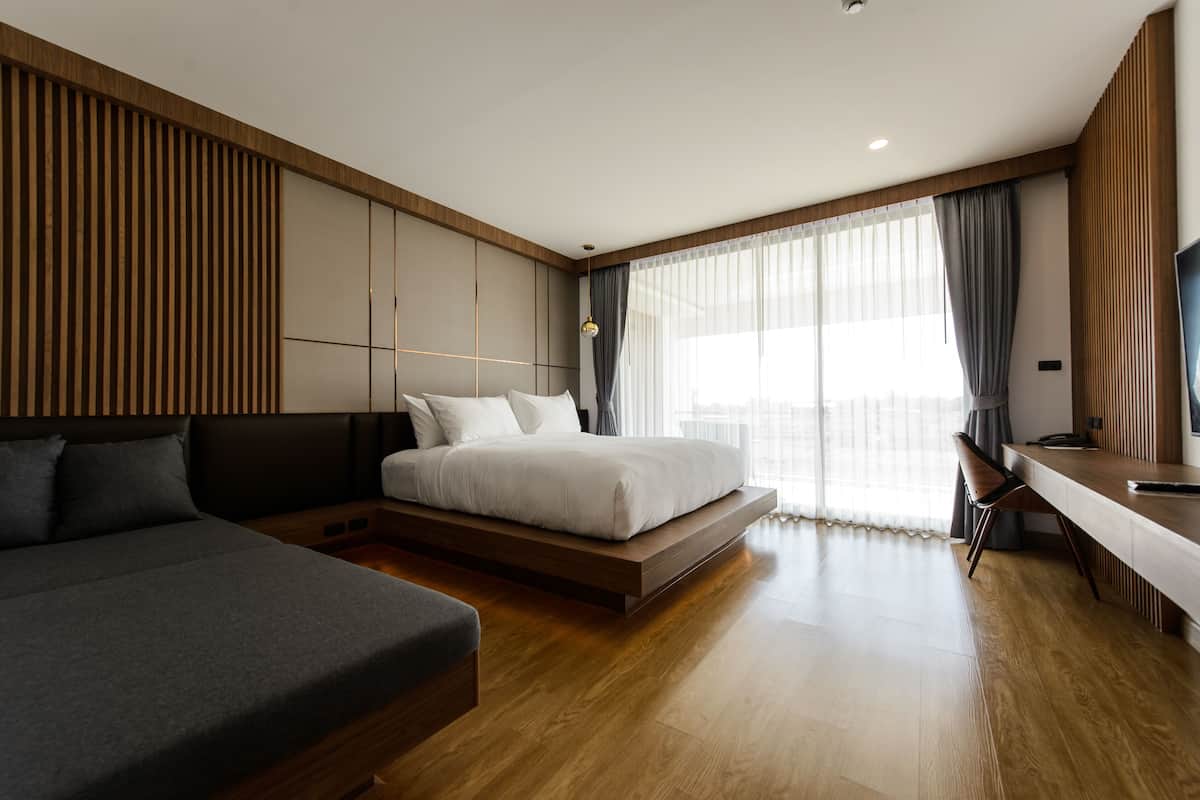 A modern hotel room with a large bed, a sofa, a desk, and a TV.