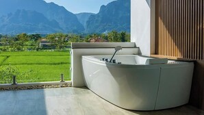 A modern bathroom with a freestanding bathtub, a wooden slat wall, and a view of a green landscape and mountains. - TEVA Valley Resort (Mae Sai)
