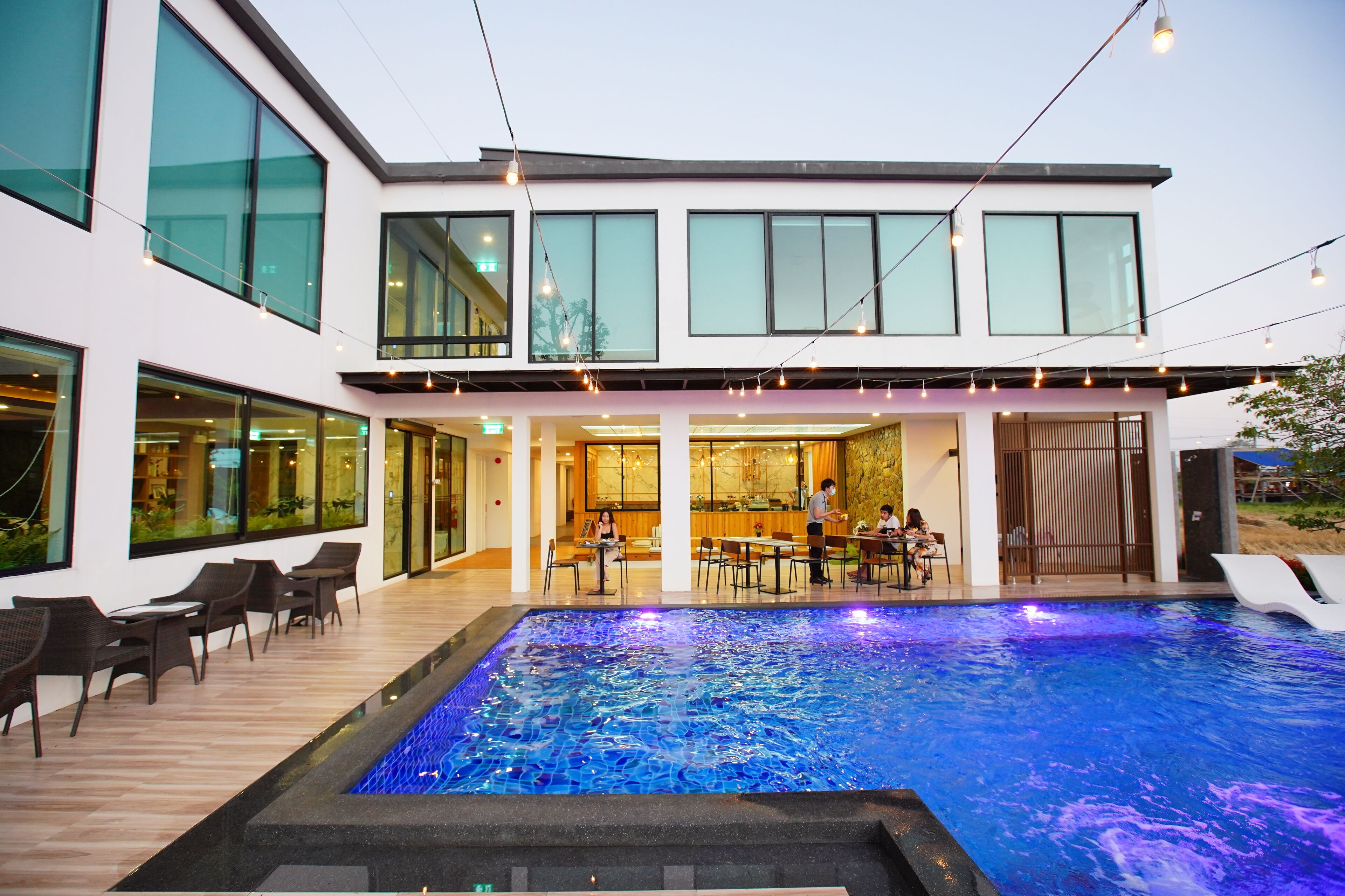 A modern building with a swimming pool, outdoor seating, and large windows.