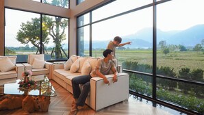 A modern living room with a large window, a sofa, and a coffee table. - TEVA Valley Resort (Mae Sai)