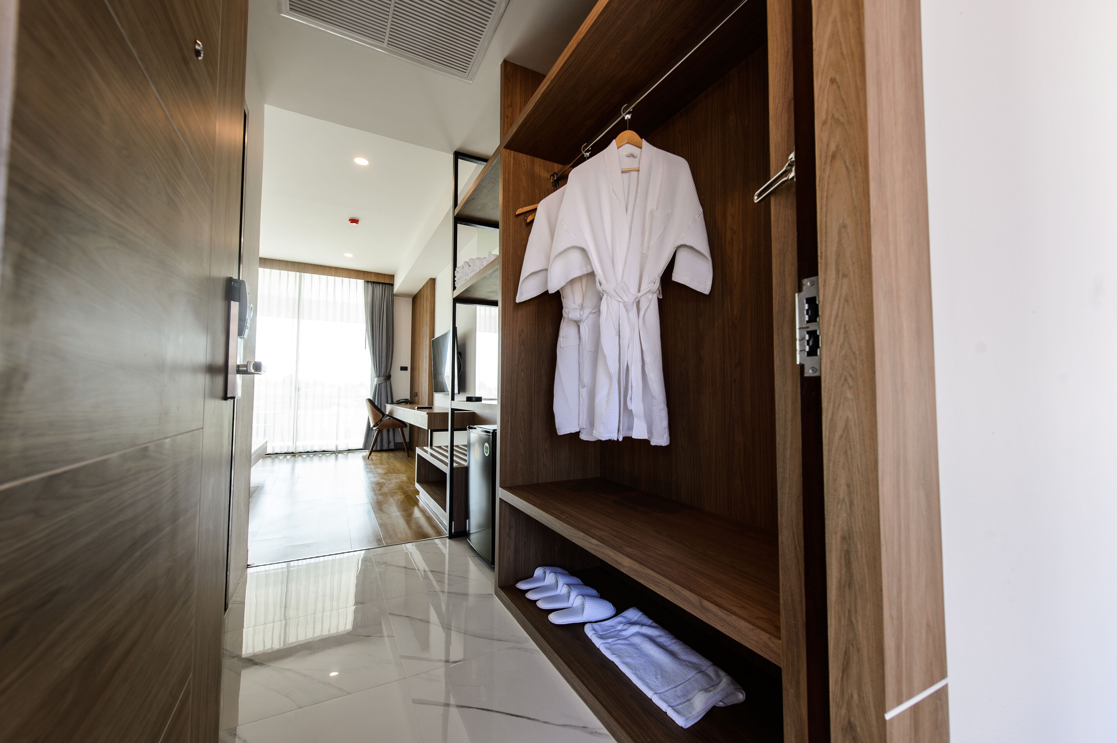 A modern hotel room with a wooden wardrobe, a robe hanging on the door, and neatly folded towels on the floor.