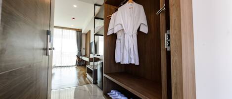A modern hotel room with a wooden wardrobe, a robe hanging on the door, and neatly folded towels on the floor.
