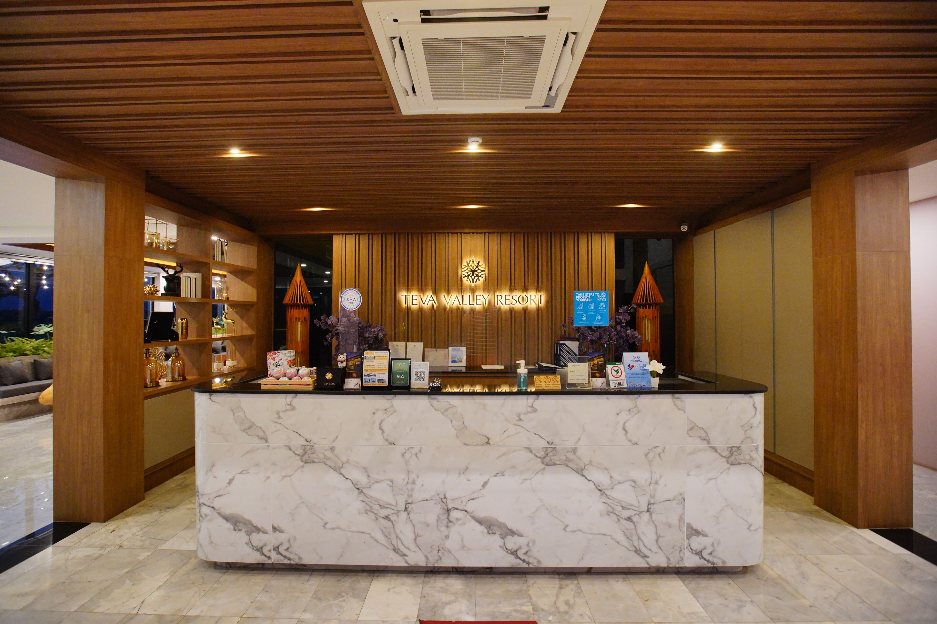Un comptoir d’accueil au Teva Valley Resort, doté d’un comptoir en marbre, de panneaux en bois et d’une enseigne au-dessus.
