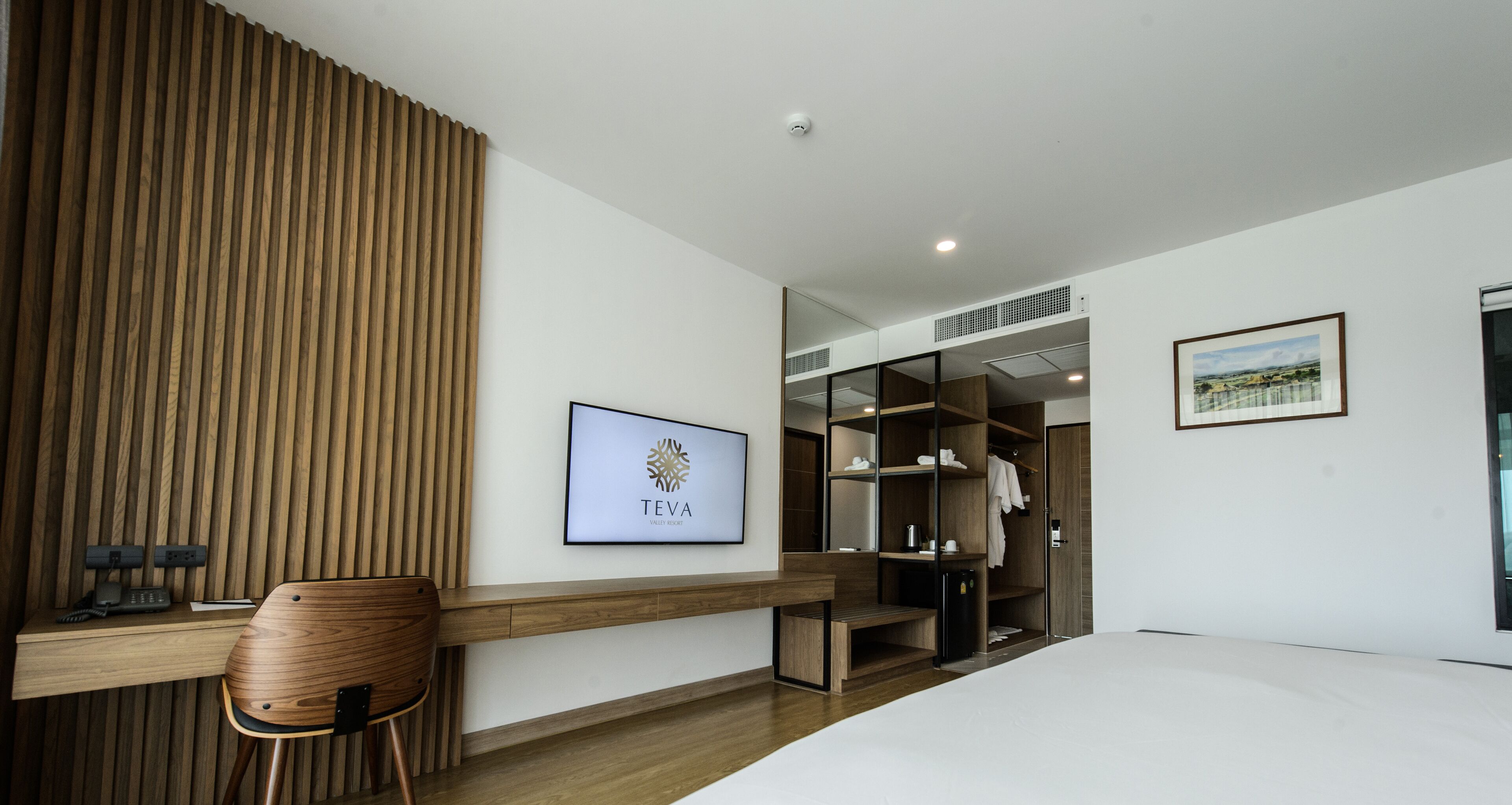 A modern hotel room with a wooden desk, a chair, a wardrobe, and a bed.
