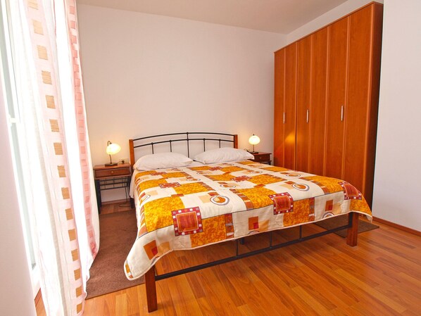 A bedroom with a bed, wooden wardrobe, nightstand, and a lamp.