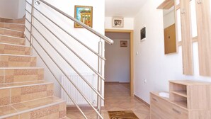 Una escalera con barandillas de metal que conduce a un pasillo con un radiador, un armario de madera y una alfombra con motivos de café.