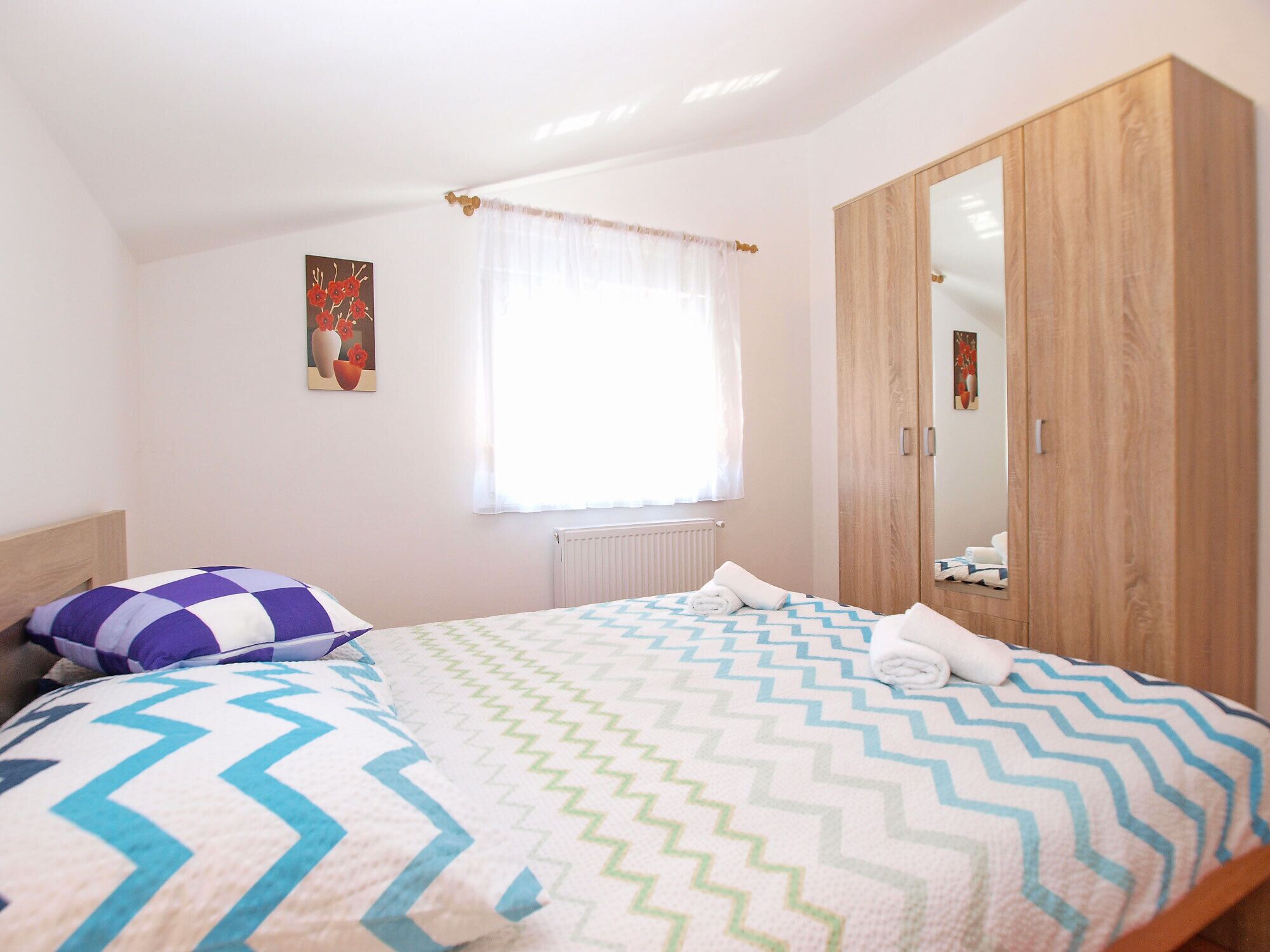 A bedroom with a bed, a wardrobe, a window with curtains, and a radiator.
