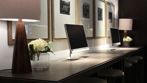 Een lange, donkere houten receptiebalie met twee monitoren, een vaas witte bloemen en een lamp.