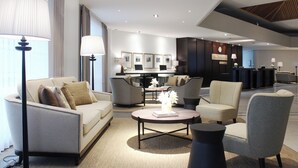 Een moderne hotelentree met een bank, fauteuils, een salontafel en een receptiebalie.
