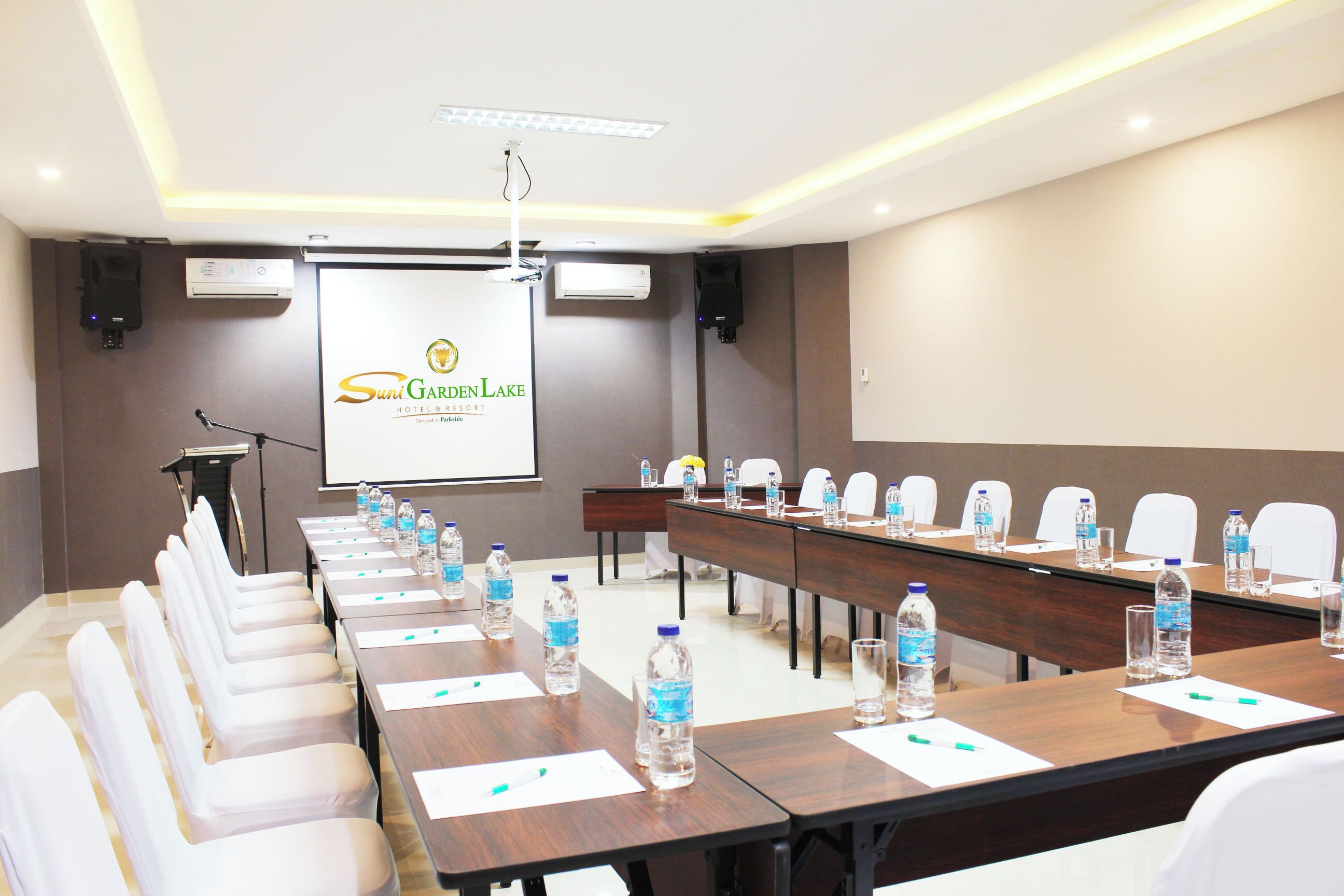 A conference room at Sun Garden Lake Hotel & Resort with a long table, chairs, water bottles, and a projector screen.