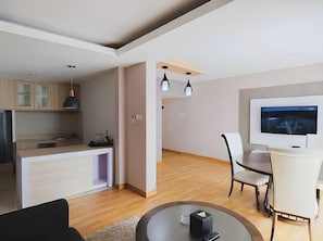 Ein modernes Wohnzimmer mit Essbereich, Küche und an der Wand befestigtem Fernseher.