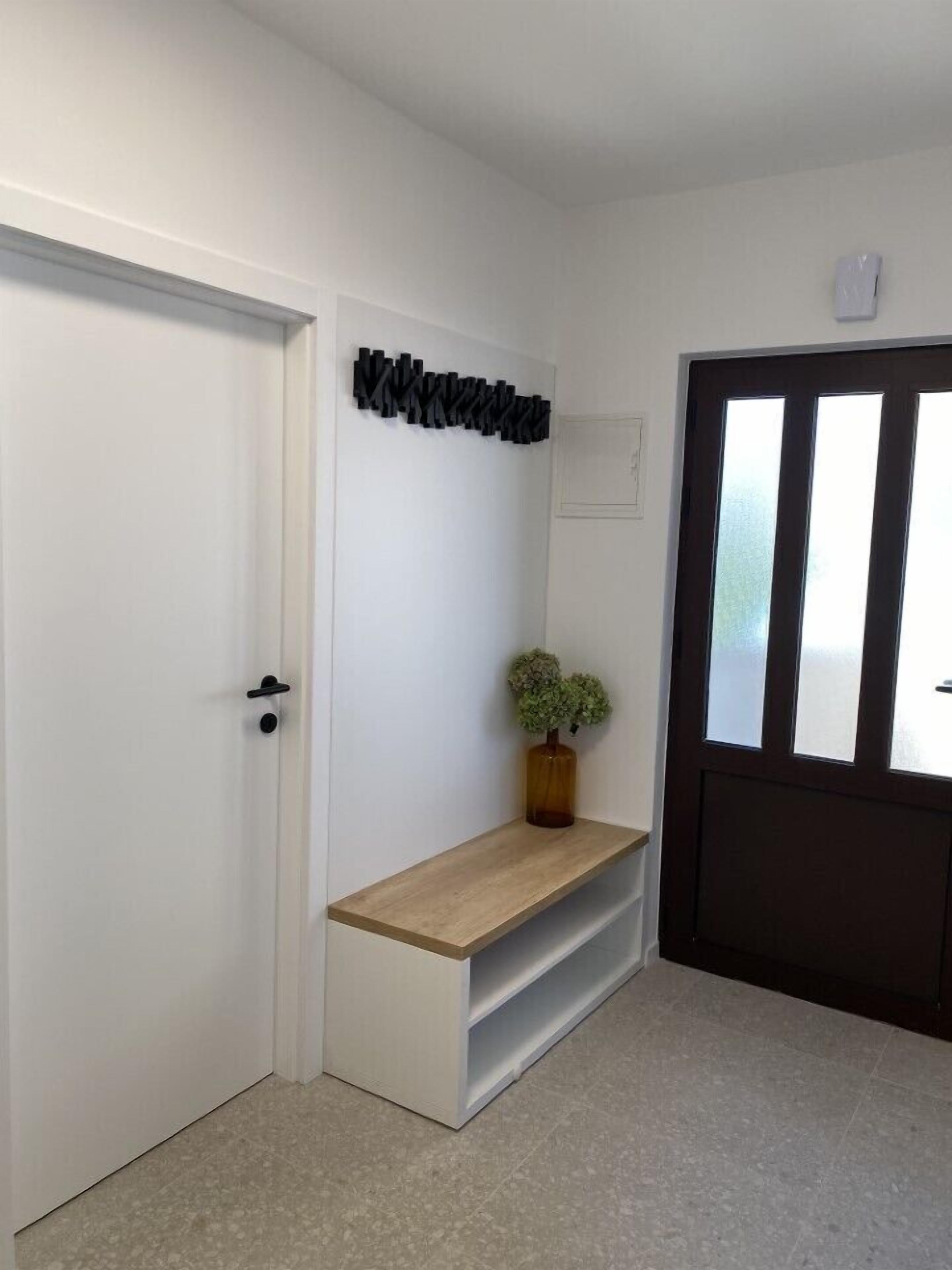 A hallway with a white door, a bench with a potted plant, and a dark door with frosted glass panels.