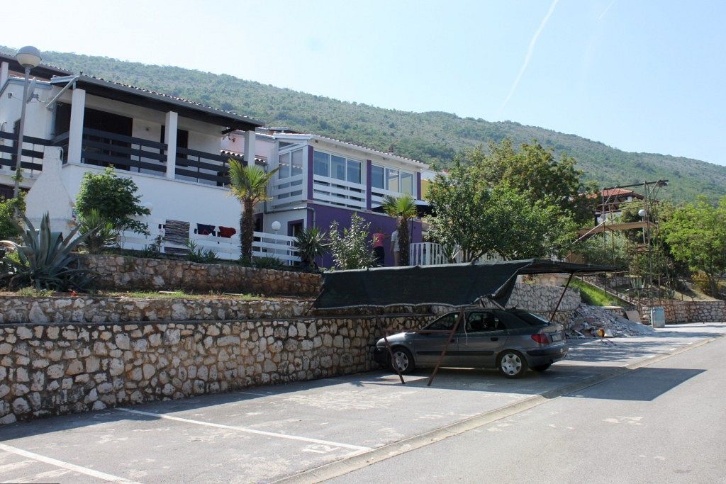 Ein Parkplatz mit Steinmauer, einem Auto und einem Mehrstöckiger Gebäude mit Balkonen.