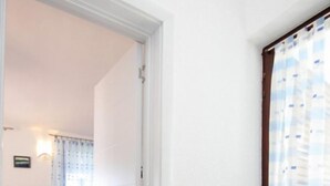 A room with a wooden floor, a bed with a blue and yellow bedspread, a white door, and a window with a blue and white curtain.