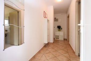 A hallway with a white door, a mirror, a white cabinet, and a potted plant.