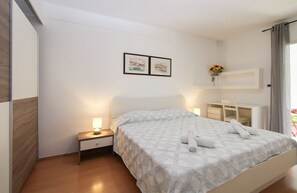 A hotel room with a bed, bedside table, lamp, and a desk with a chair.