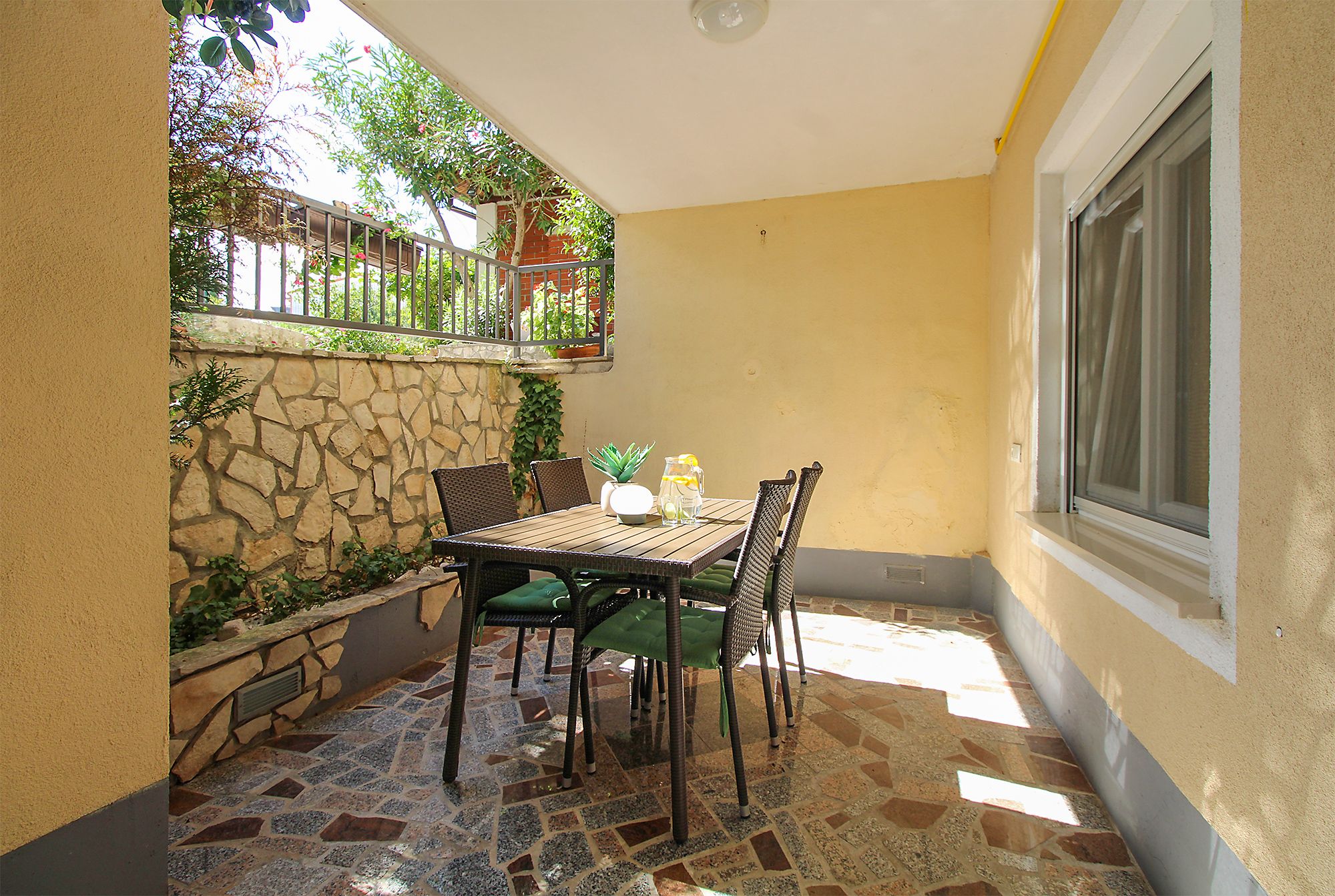 A patio with a stone wall, a table with chairs, and a window.