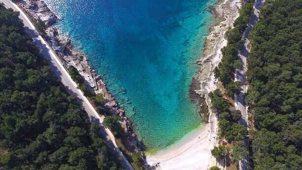An aerial view of a coastal area with a clear blue sea, a sandy beach, and dense green forest. - Apartment 1348/12669 (Istria - Pula), 100m from the beach (Pula)