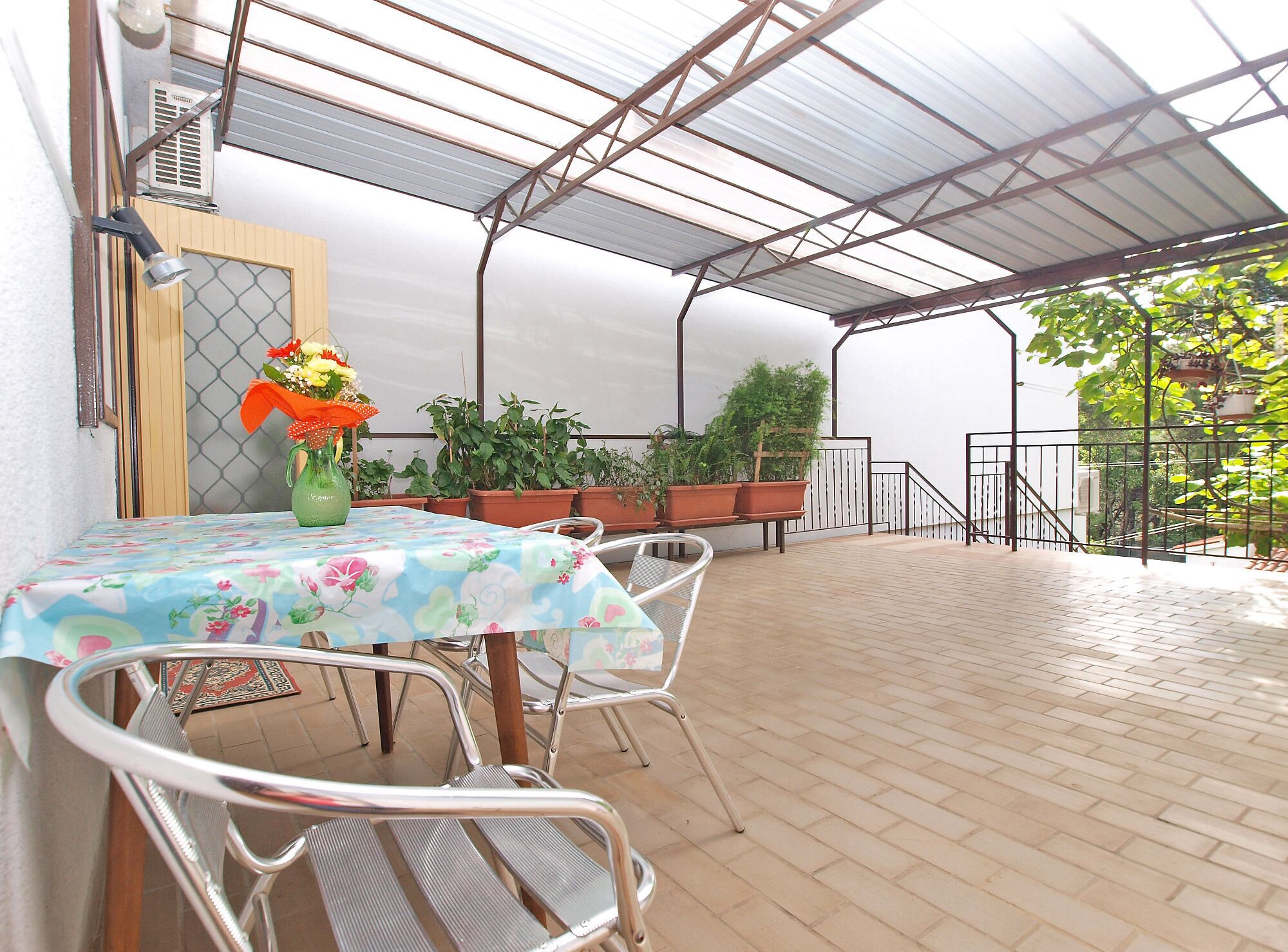 Une terrasse extérieure avec une table et des chaises, des plantes en pot et un escalier en métal.