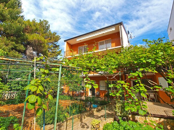 A residential building with a balcony and a garden area with various plants and a trellis.
