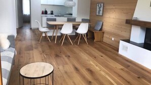 A modern kitchen with white cabinets, a dining area with a wooden table and chairs, and a cozy seating area with a round table and a sofa. - Turmalin 2. Stock by Interhome (Lenk)