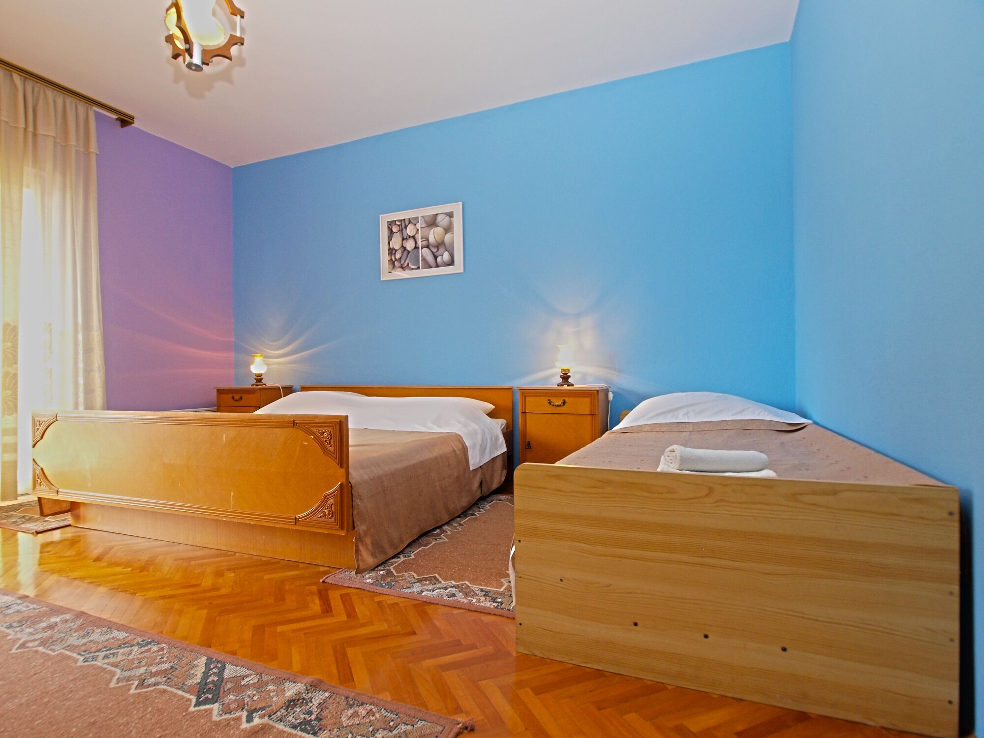 A room with two wooden beds, a blue wall, a wooden floor, and a small rug.