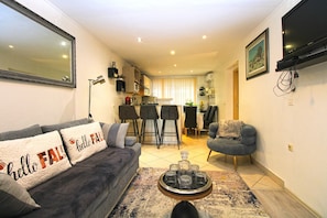 A living room with a sofa, a coffee table, a TV, and a kitchen in the background. - Apartment 1352/12718 (Istria - Pula), 750m from the beach (Pula)