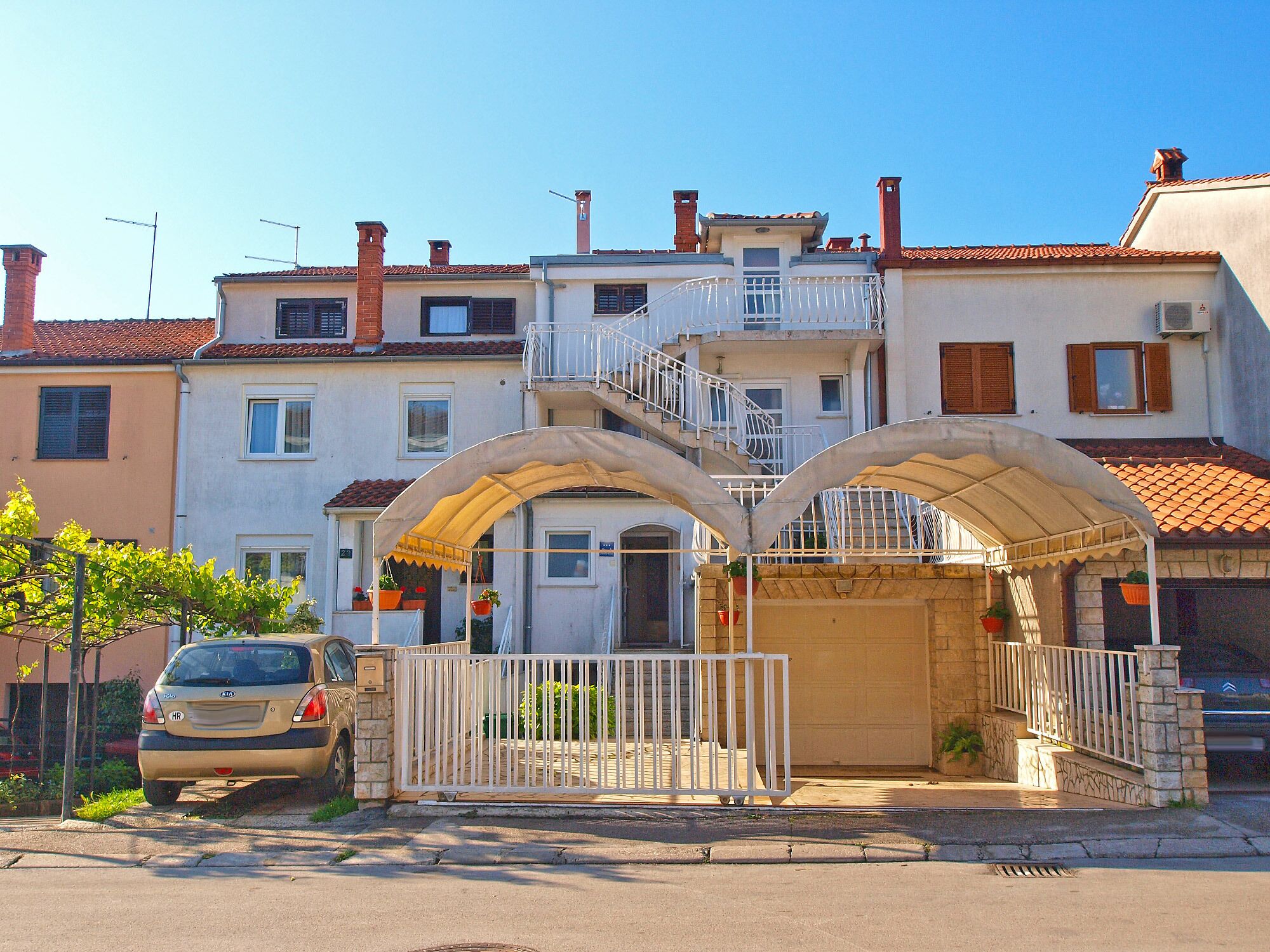 A residential building with a gated entrance, a staircase leading to an upper floor, and a car parked in front.