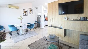 A modern living room with a flat-screen TV, a dining area with blue chairs, a kitchen in the background, and a small side table with a bowl. - Apartment 1352/12722 (Istria - Pula), 750m from the beach (Pula)