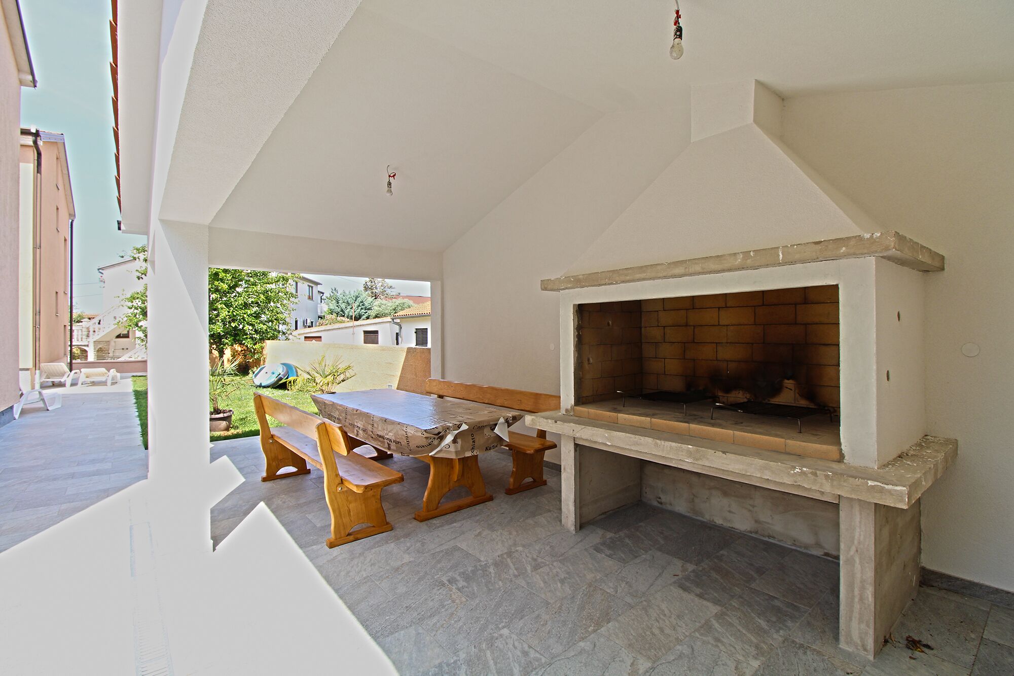 An outdoor patio with a wooden table and benches, a brick fireplace, and a view of the neighborhood.