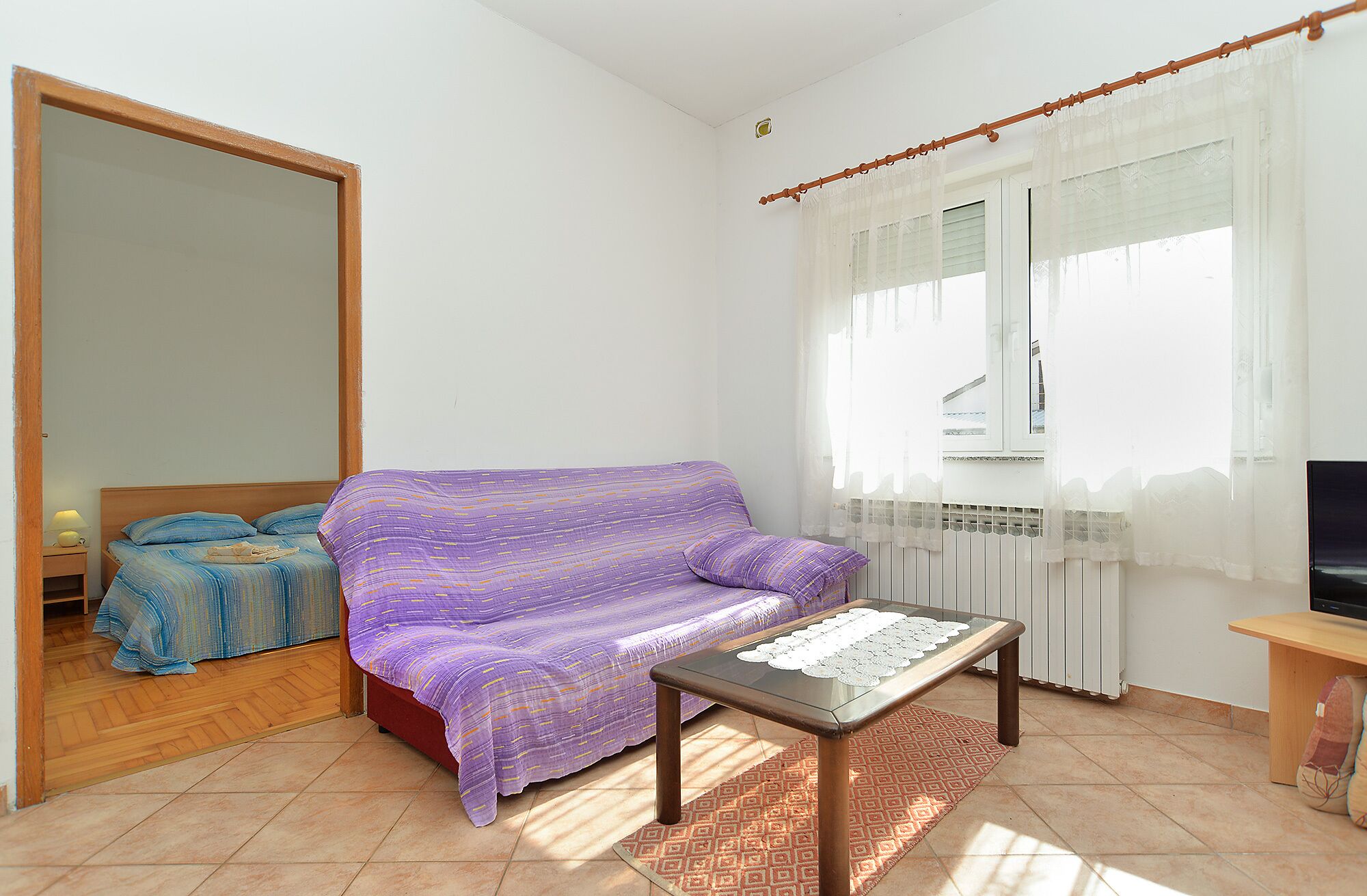 Een kleine, lichte kamer met een bank, een tafel en een bed.