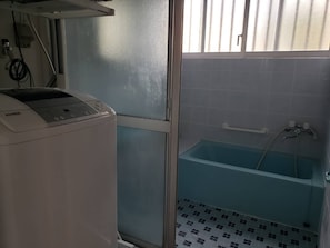 Un baño con bañera, lavadora y ventana con persianas.