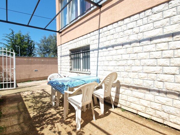 Un patio con tavolo e sedie, un muro di mattoni bianchi e un cancello in metallo.