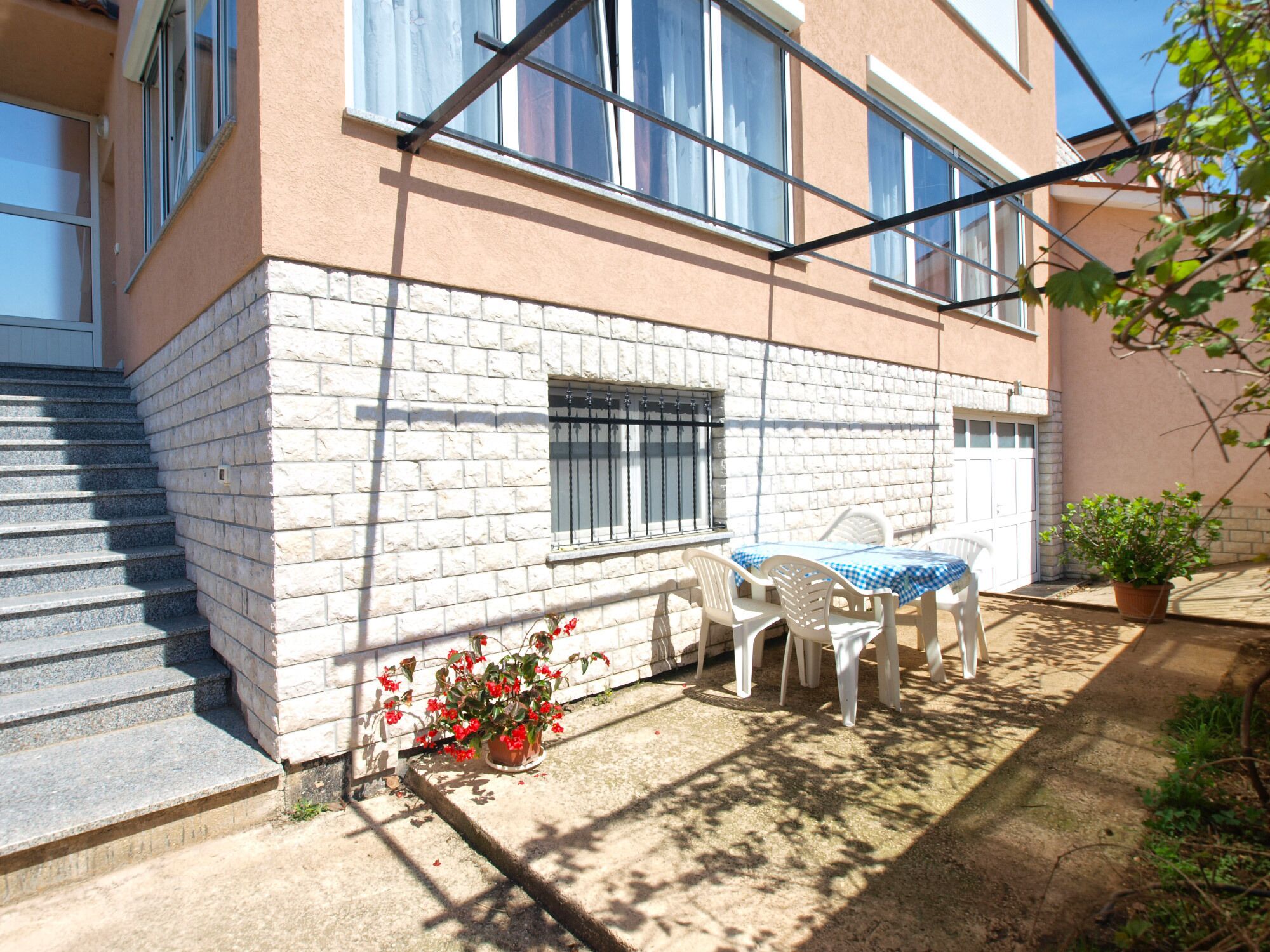 A building with a brick exterior, a set of stairs, a window with bars, a table with chairs, and a potted plant.