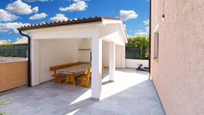 A covered patio area with a wooden bench and a table, a clear blue sky, and a stone wall in the background. - Apartment 1359/16593 (Istria - Peroj), 500m from the beach (Peroj)