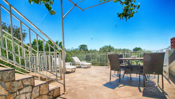 Une terrasse avec des meubles d’extérieur, un mur en pierre et une rambarde en métal.