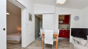 Een ruimtelijk ingerichte leefruimte met een eethoek, een kitchenette, een televisie en een bed.