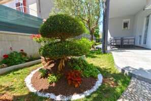 Stroll through the serene garden, surrounded by a variety of plants and a neatly trimmed topiary tree, with a patio area perfect for relaxation.